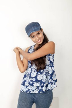 Genç ve güzel bir Hintli kadın modelin günlük spor kıyafetleri içinde beyaz arka planda mavi-beyaz bluz, mavi kot pantolon ve mavi başlık giyerken çekilmiş bir fotoğraf. Kadın manken. Moda Portresi.