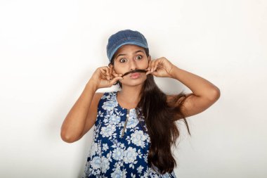 Genç ve güzel bir Hintli kadın modelin günlük spor kıyafetleri içinde beyaz arka planda mavi-beyaz bluz, mavi kot pantolon ve mavi başlık giyerken çekilmiş bir fotoğraf. Kadın manken. Moda Portresi.