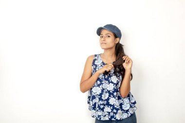 Genç ve güzel bir Hintli kadın modelin günlük spor kıyafetleri içinde beyaz arka planda mavi-beyaz bluz, mavi kot pantolon ve mavi başlık giyerken çekilmiş bir fotoğraf. Kadın manken. Moda Portresi.