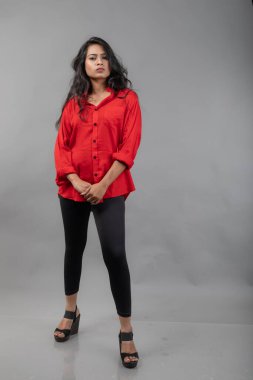 Gri arka plan karşısında gündelik giyimli Hintli genç bayan model - stok fotoğrafı. Kırmızı gömlek ve siyah kot giyen uzun siyah saçlı bir manken..