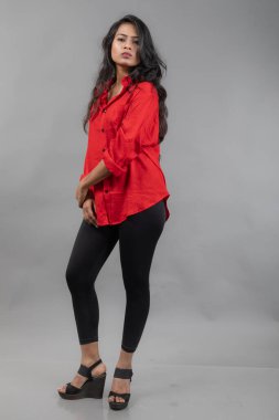 Gri arka plan karşısında gündelik giyimli Hintli genç bayan model - stok fotoğrafı. Kırmızı gömlek ve siyah kot giyen uzun siyah saçlı bir manken..