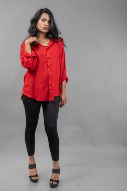 Gri arka plan karşısında gündelik giyimli Hintli genç bayan model - stok fotoğrafı. Kırmızı gömlek ve siyah kot giyen uzun siyah saçlı bir manken..