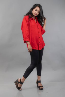 Gri arka plan karşısında gündelik giyimli Hintli genç bayan model - stok fotoğrafı. Kırmızı gömlek ve siyah kot giyen uzun siyah saçlı bir manken..