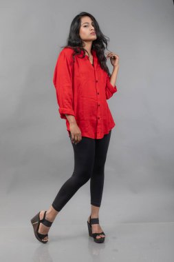 Gri arka plan karşısında gündelik giyimli Hintli genç bayan model - stok fotoğrafı. Kırmızı gömlek ve siyah kot giyen uzun siyah saçlı bir manken..