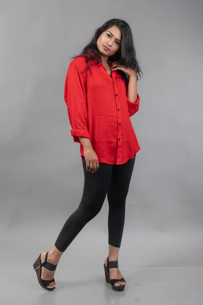 Indian young female model in casual wear against grey background - stock photo. Long black haired model wearing red shirt and black jeans.