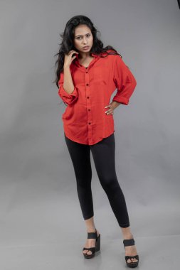 Gri arka plan karşısında gündelik giyimli Hintli genç bayan model - stok fotoğrafı. Kırmızı gömlek ve siyah kot giyen uzun siyah saçlı bir manken..