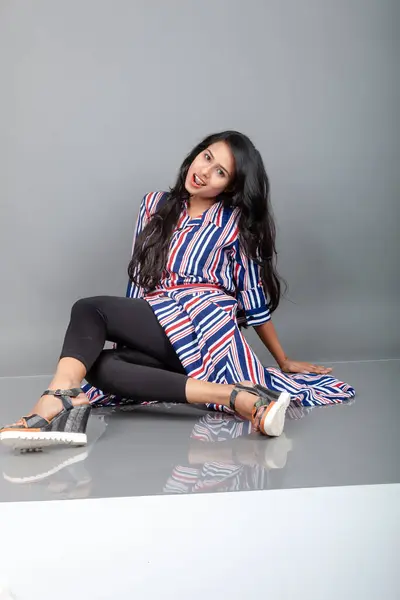 Beautiful woman wearing heeled sandals, black leggings and red, blue, white striped tunic. Female model showing footwear product, advertisement shot.
