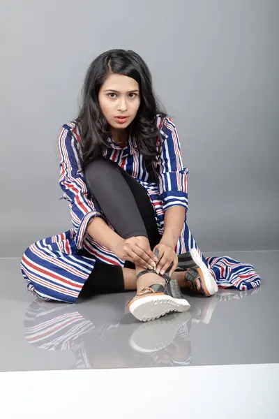 Beautiful woman wearing heeled sandals, black leggings and red, blue, white striped tunic. Female model showing footwear product, advertisement shot.