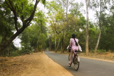 Mukutmanipur, Bankura, Batı Bengal - 7 Nisan 2017: Bir yaz sabahı erken saatlerde, yeşil bir ormanda, yalnız bir yolda bisiklet süren, pembe salwar giyen bir köy kızı