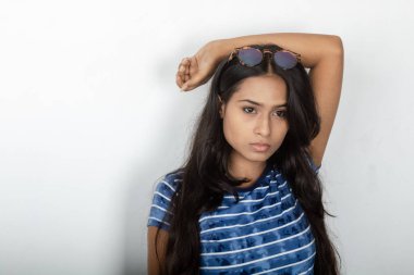 Genç ve güzel bir Hintli kadın modelin günlük kıyafetleri içinde, mavi ve beyaz baskılı bluzu ve beyaz arka planda temiz bir gözlüğü var. Reklam çekimi. Göz ürünü çekimi.