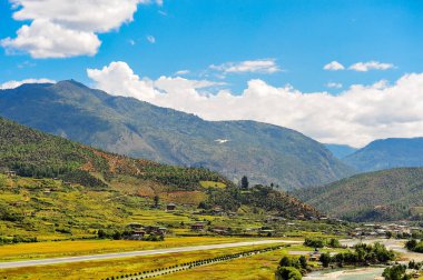 Havaalanı ve Paro Vadisi 'nin panoramik manzarası, Butan. Dağ, nehir, yeşil çayırlar ve tarım arazisi ile manzara, beyaz bulutlu mavi gökyüzü.