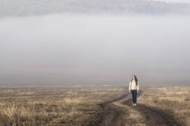 Sisli zemin yolu kırsal kesimde sisli yollarla dolu. Sabah erken saatlerde yürüyen kız çocukları. Sis Sonbaharı. Minimalist yalnız gün doğumu Sisli hava güzel
