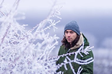 close up frost man male young 30 years old long hair snow  a winter day forest  branches hoarfrost concept green coat  park cold snow nature gray hat outdoors snowy Moldova..