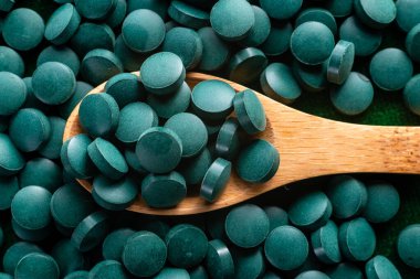 Green Organic Spirulina in algae pills tablets  bamboo wood  spoon rich in iron Close-up Super food concept healthy.