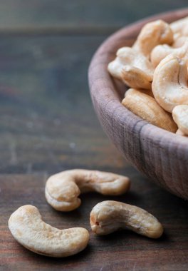 Çiğ kaju ve organik fındıklı kase ahşap masa, sade vejetaryen atıştırmalık Hint cevizi anacardium bataklık kumaşı yakın plan.