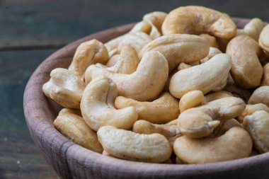 Çiğ kaju ve organik fındıklı kase ahşap masa, sade vejetaryen atıştırmalık Hint cevizi anacardium bataklık kumaşı yakın plan.