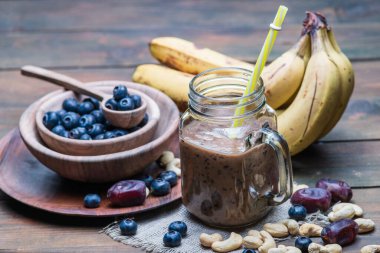 Böğürtlen karışımı olgun muzlu meyve suyu mor meyve suyu, milkshake karışımı sağlıklı yüksek proteinli, lezzetli cam, sabah bölümü ahşap fındıklı kaju ağacında.