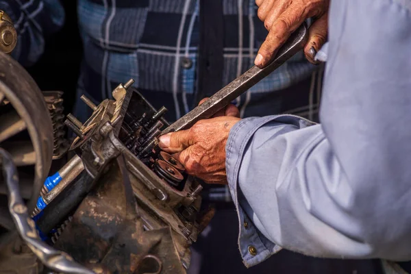Two old men Auto mechanic working on car rusty engine in mechanics garage. Repair service close-up wrinkled dirty hands blue clothes Gear truck  Disassemble wrench home