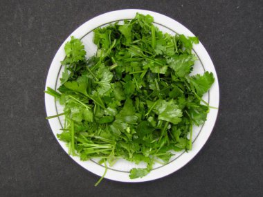 Kişniş yaprakları siyah arkaplanda bir tabakta 