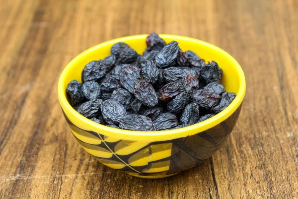 Kurumuş siyah kuru üzümler ahşap arka planda bir kasede 