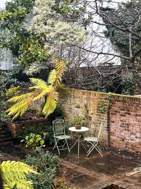 Cozy inner garden on Notting Hill in London. A small garden table and cute green chairs are located in the middle, surrounded by fabulous greenery.