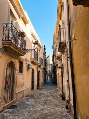 Narrow streets on the old town of Syracuse in Sicily, Italy. Gorgeous architecture in the sunshine. Scooters are parked near the walls, and greenery is in the pots.