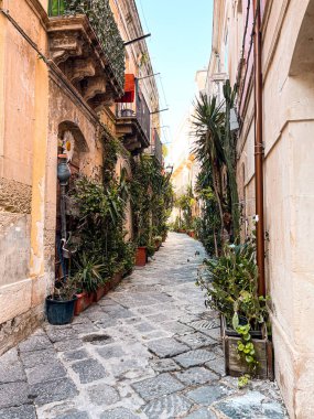 Narrow streets on the old town of Syracuse in Sicily, Italy. Gorgeous architecture in the sunshine. Scooters are parked near the walls, and greenery is in the pots.