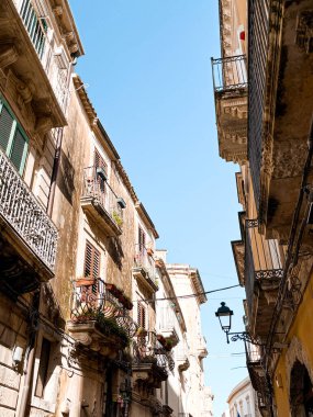 Narrow streets on the old town of Syracuse in Sicily, Italy. Gorgeous architecture in the sunshine. Scooters are parked near the walls, and greenery is in the pots.