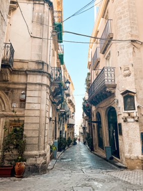 Narrow streets on the old town of Syracuse in Sicily, Italy. Gorgeous architecture in the sunshine. Scooters are parked near the walls, and greenery is in the pots.