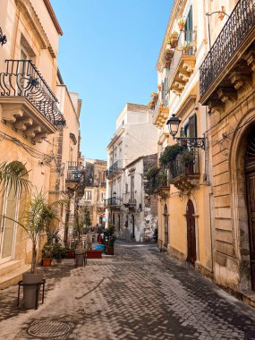 Narrow streets on the old town of Syracuse in Sicily, Italy. Gorgeous architecture in the sunshine. Scooters are parked near the walls, and greenery is in the pots.
