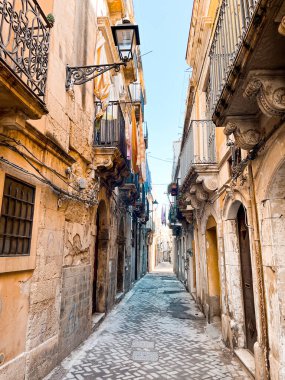 Narrow streets on the old town of Syracuse in Sicily, Italy. Gorgeous architecture in the sunshine. Scooters are parked near the walls, and greenery is in the pots.