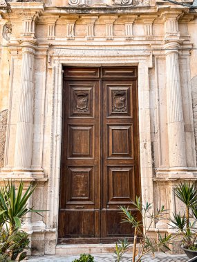 Old wooden doors in the ancient wall, placed in-between columns. Green plants around make the architecture look order and more pleasant. History lives in these doors