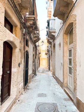 Narrow streets on the old town of Syracuse in Sicily, Italy. Gorgeous architecture in the sunshine. Scooters are parked near the walls, and greenery is in the pots.