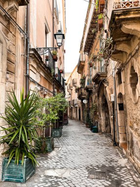 Narrow streets on the old town of Syracuse in Sicily, Italy. Gorgeous architecture in the sunshine. Scooters are parked near the walls, and greenery is in the pots.