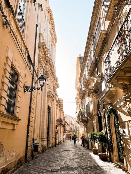 Narrow streets on the old town of Syracuse in Sicily, Italy. Gorgeous architecture in the sunshine. Scooters are parked near the walls, and greenery is in the pots.
