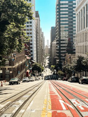 San Francisco 'daki tepenin tepesinden bak. Yolun ortasında, yolun aşağısına giden tramvay korkulukları var. Ufuktaki gökdelenler ve asma köprü.