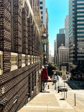 San Francisco 'daki tepenin tepesinden bak. Yolun ortasında, yolun aşağısına giden tramvay korkulukları var. Ufuktaki gökdelenler ve asma köprü.