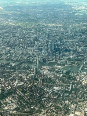 Londra 'nın havadan görünüşü. Uçağın penceresinden Londra şehir merkezinin görüntüsü. Şehrin üzerinde mavi ve gri manzaralarla uçuyor. Nehir manzarası ve gökdelenler.