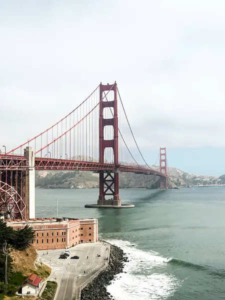 San Francisco 'daki Golden Gate köprüsünün kıyı manzarası. Amerikan simgesi. Uçurumlar ve çimenler resmi çerçeveliyor. Körfez suyunda dalgalar. Hafif sis.