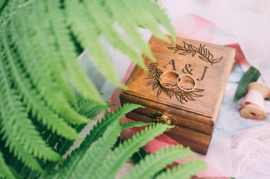 Ahşap kutuda alyanslar ve yeşil eğrelti otu yaprakları, yakın plan.   