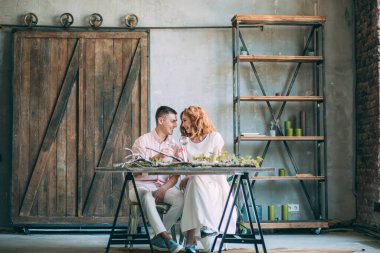 Birbirine aşık genç bir çift tahta masada oturuyor ve ellerinde bardaklarla.          
