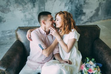 Genç ve güzel gelin ve damat bir kanepede oturuyor ve stüdyoda sarılıyorlar.          