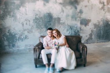 Genç ve güzel gelin ve damat bir kanepede oturuyor ve stüdyoda sarılıyorlar.          