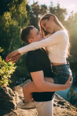 Mutlu genç çift göl kenarında sarılıyor ve gülümsüyor.             