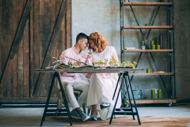 Birbirine aşık genç bir çift tahta masada oturuyor ve ellerinde bardaklarla.          