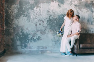 Genç ve güzel gelin ve damat bir kanepede oturuyor ve stüdyoda sarılıyorlar.          