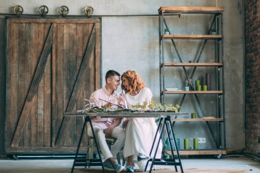 Birbirine aşık genç bir çift tahta masada oturuyor ve ellerinde bardaklarla.          