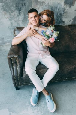 Kanepede oturan mutlu genç adam ve elinde buket tutan beyaz elbiseli kadın.