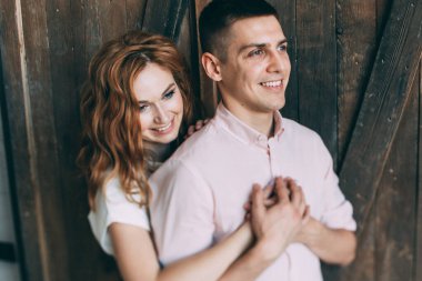 Mutlu genç çift ahşap kapının önünde sarılıp gülümsüyor.      