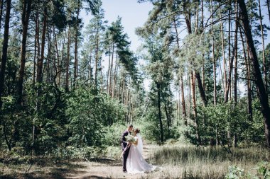 Mutlu genç bir çift ormanda yürüyor ve gülümsüyor. Buketli gelin        